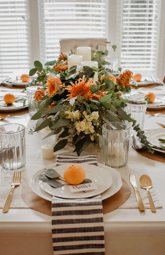 bright fall blooms with greenery and candles paired with bright citrus on the place settings are amazing for a modern Thanksgiving table
