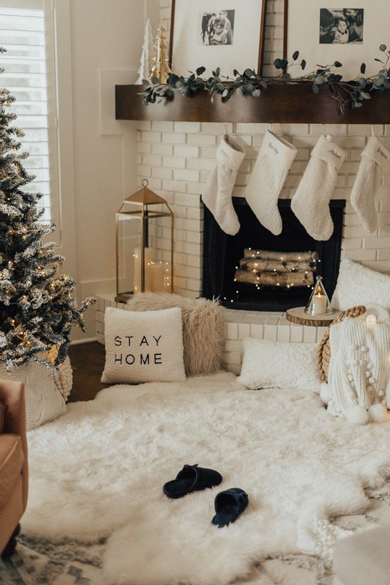 cozy winter holiday decor with white faux fur, white pillows and blankets, a greenery garland, white sotckings and a flocked Christmas tree