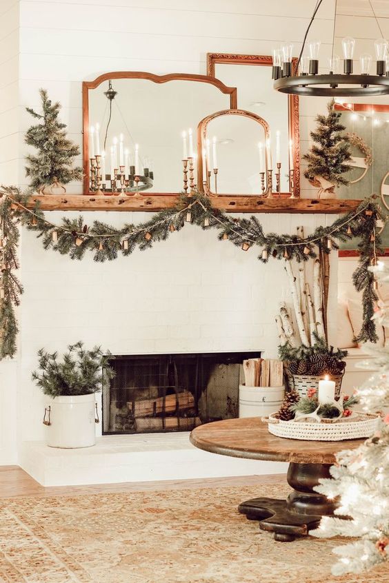 elegant rustic holiday decor with candles, a fir and bell garland, mini trees, branches in a bucket is very chic