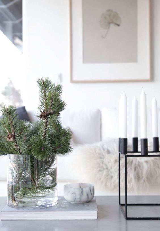 evergreen branches in a large clear vase and a modenr blakc metal candelabra with white candles for a minimal look