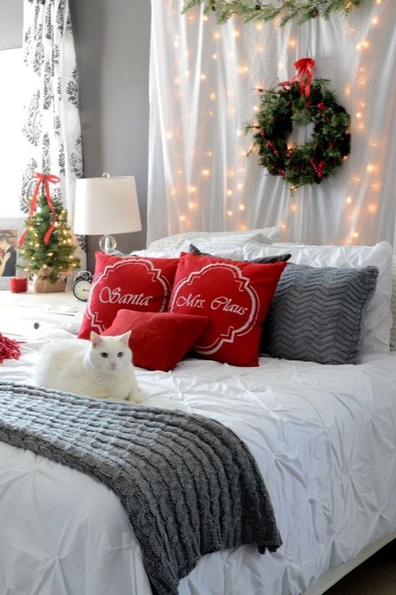 red pillows, an evergreen wreath with a red bow, lights, knit bedding and a mini Christmas tree with a red bow for a festive look