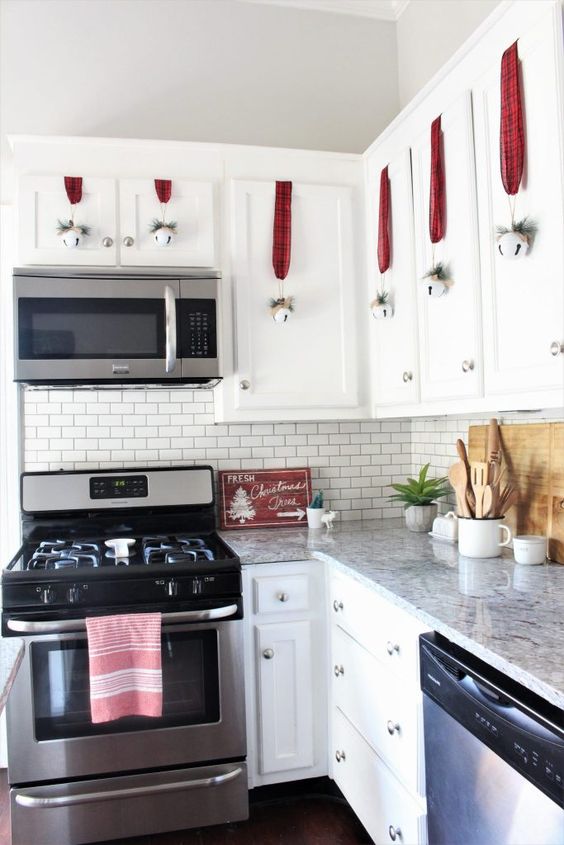 whitewashed bells with plaid ribbons and evergreens mark the cabinets and create a holiday feel in the kitchen