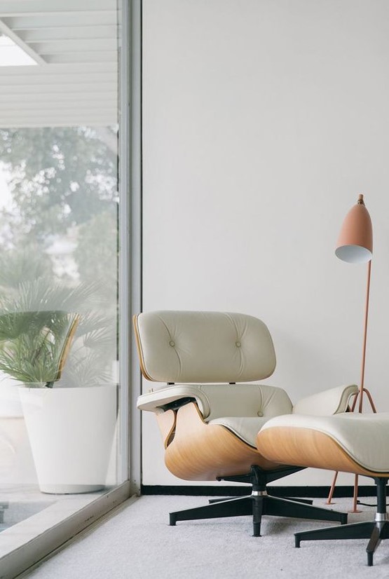 Eames lounge chair of plywood and white leather and a matching footrest by the window