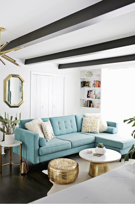a beautiful mid-century modern living room with a fireplace, dark beams on the ceiling, a modern turquoise sofa and touches of gold for more elegance