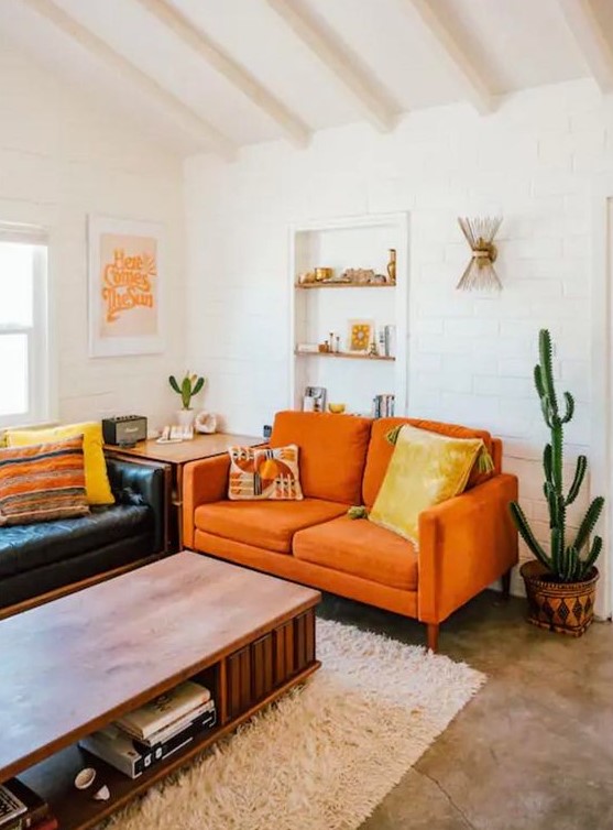 a boho living room with a black leather sofa, a modern orange loveseat, a low table and potted cacti feels warm and cool