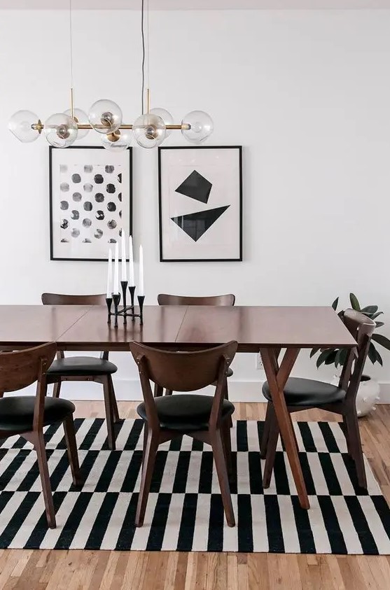 a bold black and white mid-century modern dining space with a stained table and black chairs, a striped rug and a gallery wall