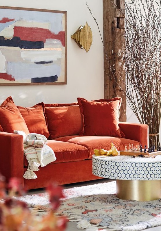 a bright living room with an orange sofa, a round table, a bold artwork and blooming branches arranged for decor