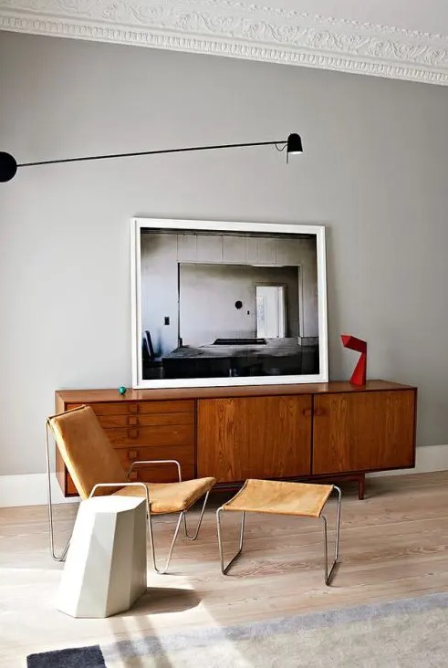a catchy space with a stained credenza, a leather chair with a footrest, a scultural side table and an artwork