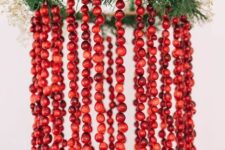 a chandelier with evergreens and white blooms plus cranberry garlands hanging down is a cool Christmas decoration