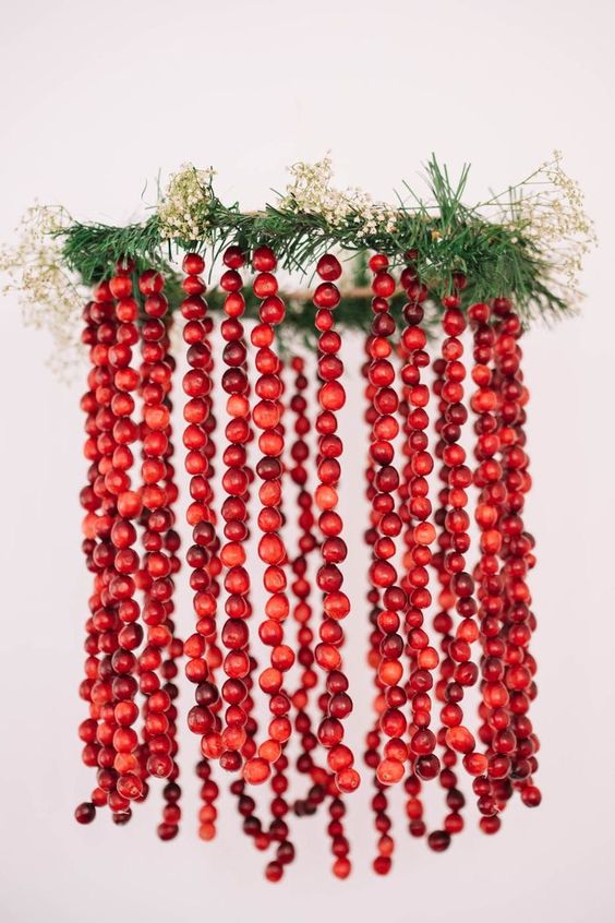 a chandelier with evergreens and white blooms plus cranberry garlands hanging down is a cool Christmas decoration