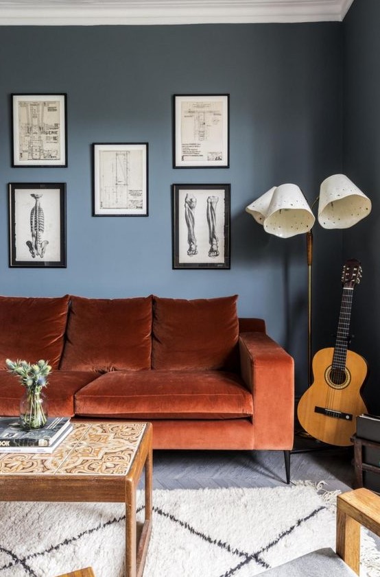 a chic living room with navy walls, a rust-colored mid-century modern sofa, a gallery wall , a floor lamp and low table with tiles is wow