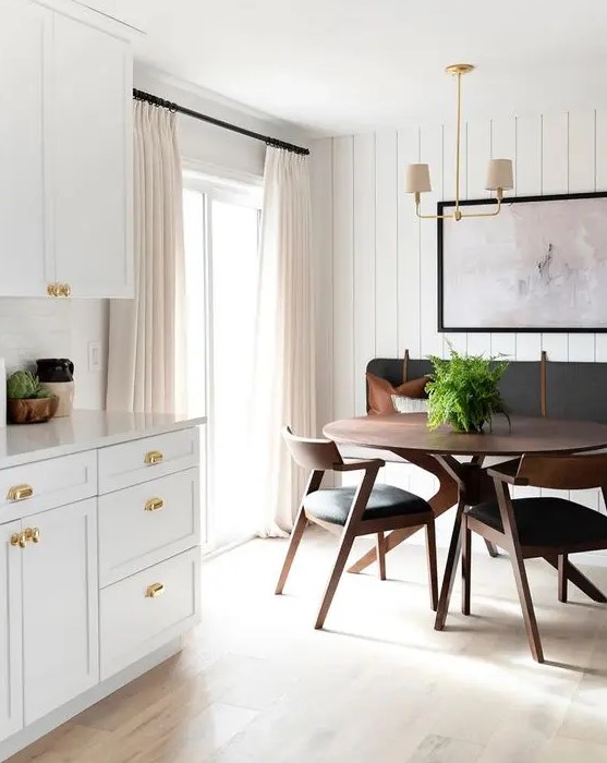 a chic mid-century modern dining nook with a built-in bench, a round stained table and black chairs, a laconic chandelier and an artwork