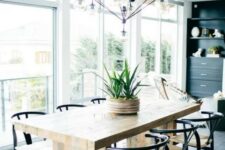 a chic mid-century modern dining space with a stained table and black and white chairs, a printed rug, a black storage unit and a large and cool chandelier