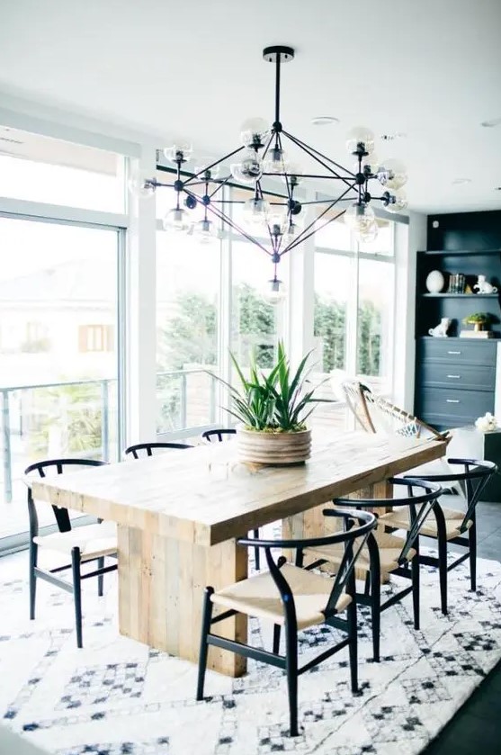 a chic mid-century modern dining space with a stained table and black and white chairs, a printed rug, a black storage unit and a large and cool chandelier