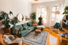 a chic mid-century modern living room with a green sectional, a rust-colored rocker, a rattan stool, statement potted plants