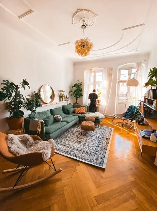 a chic mid-century modern living room with a green sectional, a rust-colored rocker, a rattan stool, statement potted plants