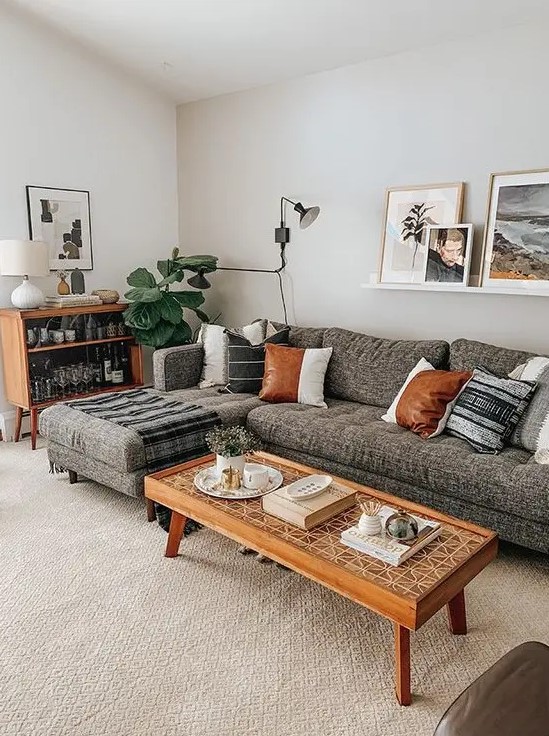 a chic mid-century modern living room with a grey sectional, stained furniture, potted plants, a gallery wall on a ledge is very cozy