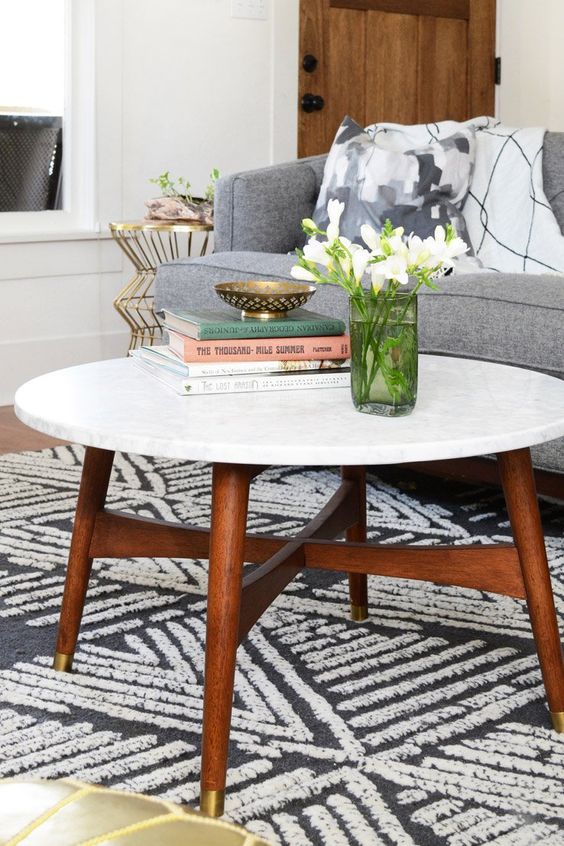 a cool mid-century modern coffee table with a white stone tabletop and rich-stained legs and a base with gold ends is amazing