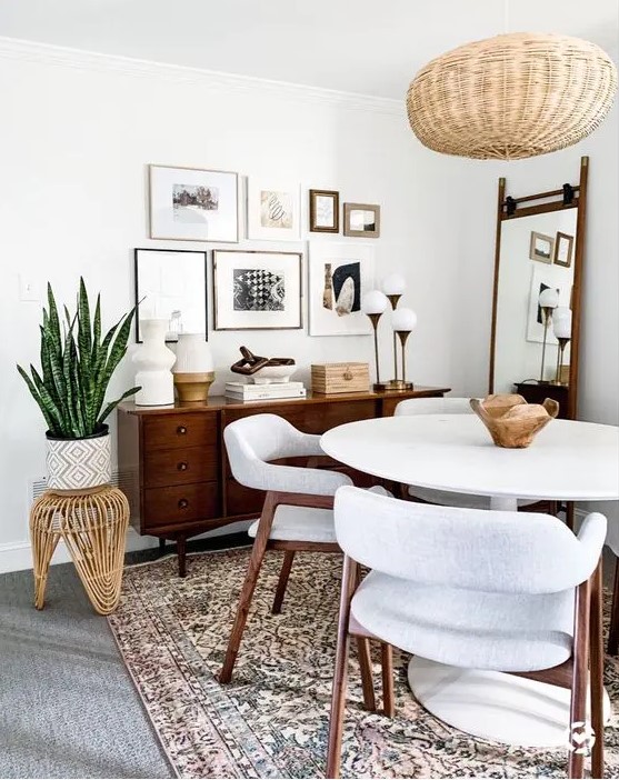 a cozy mid century modern dining nook with a stained credenza, a white round table and chairs, a woven pendant lamp and a gallery wall