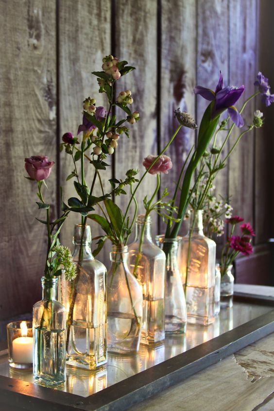 a framed mirror with vintage bottles and bright blooms plus candles is a cool decoration for any rustic or boho space