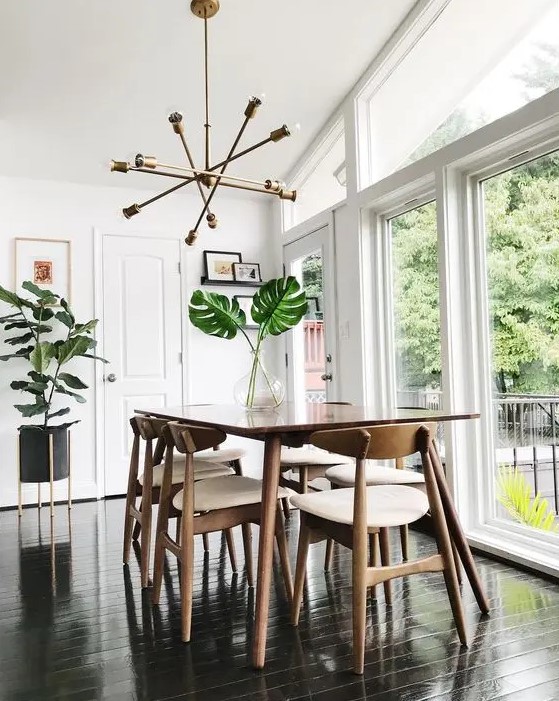 a fresh and light filled mid century modern dining space with a stained table, white chairs, a gold chandelier and potted plants