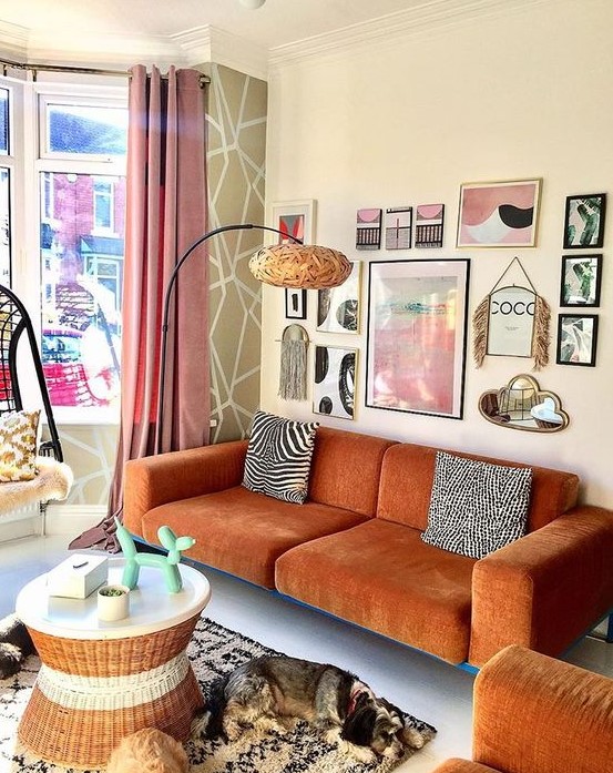 a gorgeous eclectic living room with a modern rust-colored sofa and a matching chair, a round table, a pretty gallery wall and a floor lamp