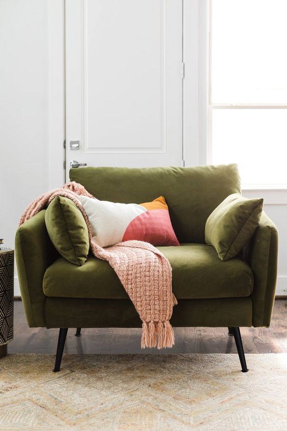 a green mid century modern chair with pillows and tall metal legs, with a woven blanket and a printed pillow is a cool and cozy idea