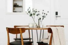 a laconic mid-century modern dining room with a mirror, a round hairpin leg table, black chairs, a black pendant lamp and thistles