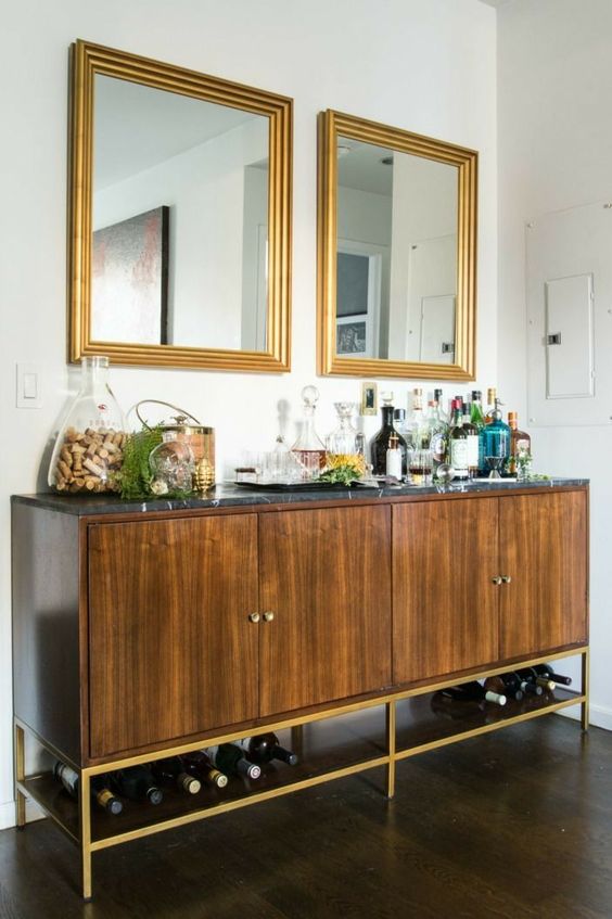 a large stained cabinet with a black stone countertop and gold base is a chic idea for a home bat, with plenty of storage space