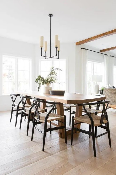 a light-filled neutral dining room with a stained table, woven chairs and a chic mid-century modern chandelier and greenery in a vase