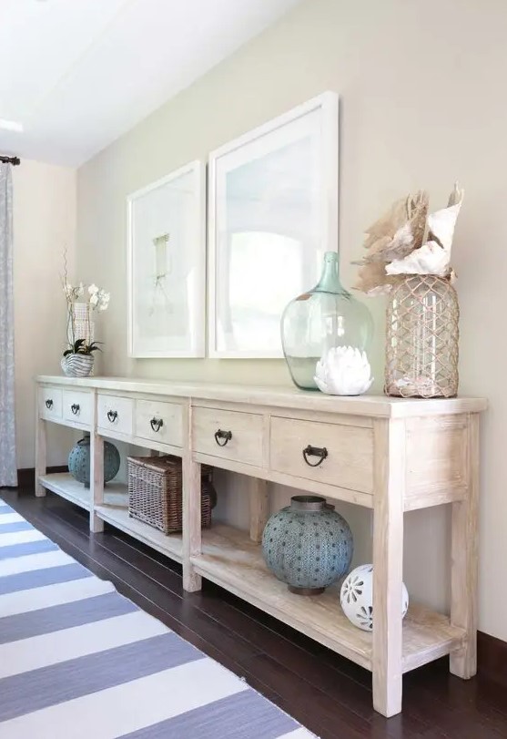 a long whitewashed console with sea-inspired artworks, large bottles and lanterns and shells