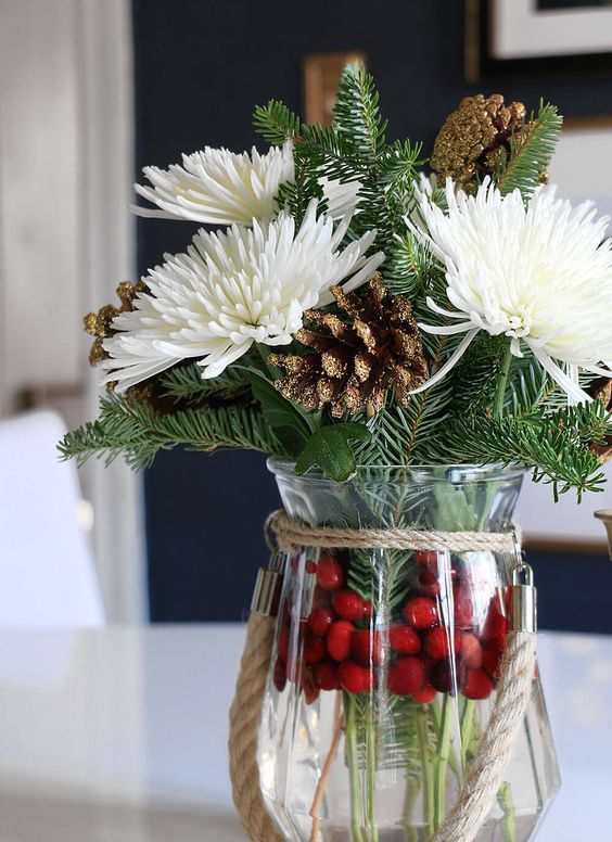 a lovely Christmas centerpiece of a vase with cranberries, evergreens, white blooms and gilded pinecones is easy to make