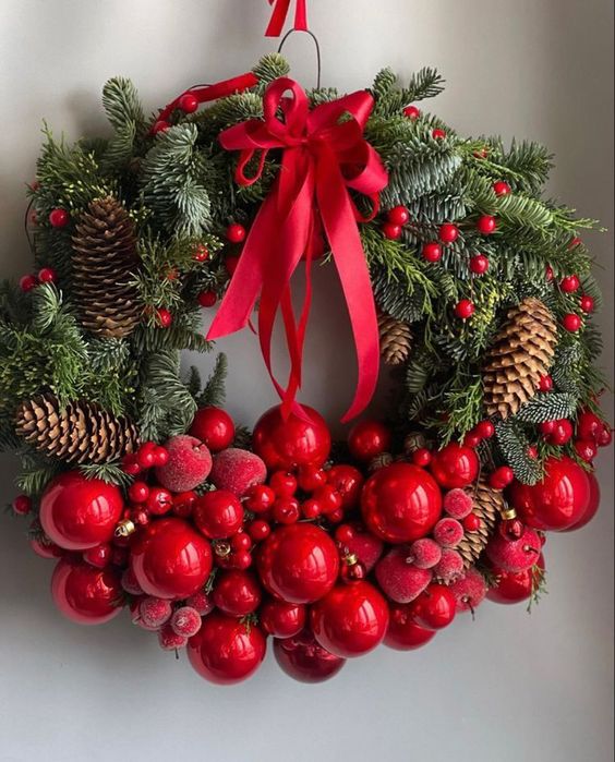 a lovely Christmas wreath of evergreens, cranberries, red ornaments and sugared apples, pinecones and a large red bow on top is a bold and cool idea