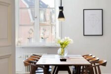 a lovely and simple mid-century modern dining space with a printed rug, a stained table and chairs, a black pendant lamp and a print