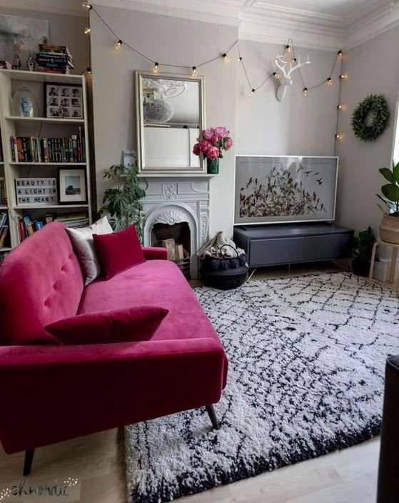 a lovely contemporary neutral living room with built-in shelves, a non-working fireplace, a hot pink loveseat, potted plants and a cool gallery wall