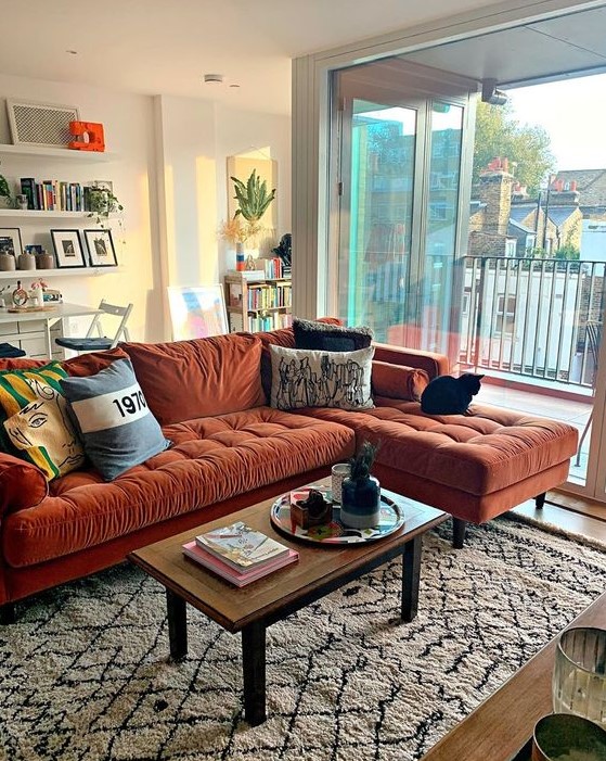 a lovely living room with a rust-colored mid-century modern sectional, a low table, floating shelves and potted plants here and there