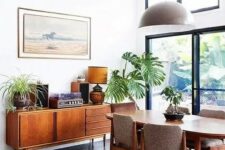 a lovely mid-century modern dining space with a stained table, grey chairs, a credenza and some plants plus a round jute rug