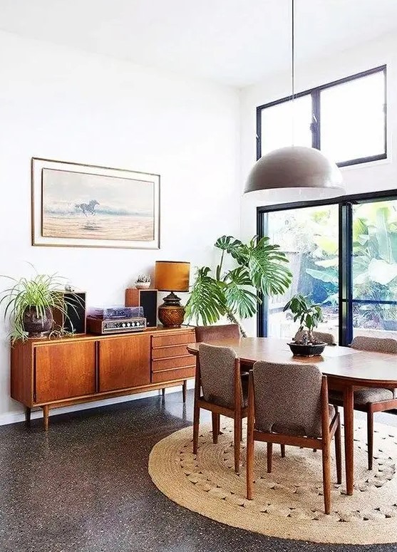 a lovely mid century modern dining space with a stained table, grey chairs, a credenza and some plants plus a round jute rug