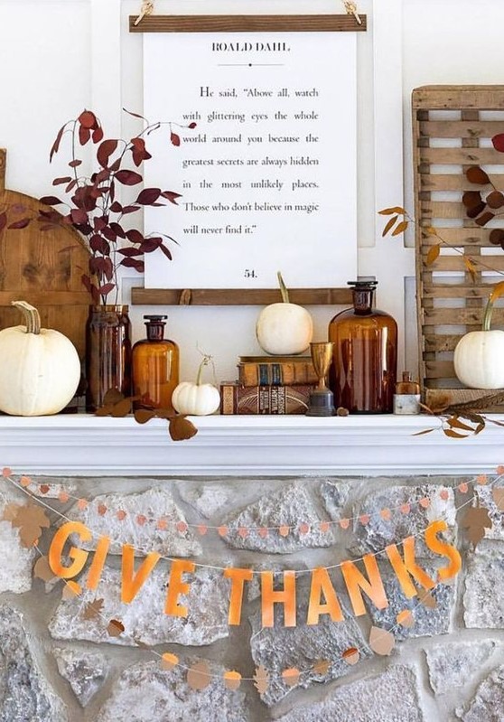 a lovely rustic fall or Thanksgiving mantel with white pumpkins, dark foliage, a sign, some wooden cutting boards and paper buntings is cool