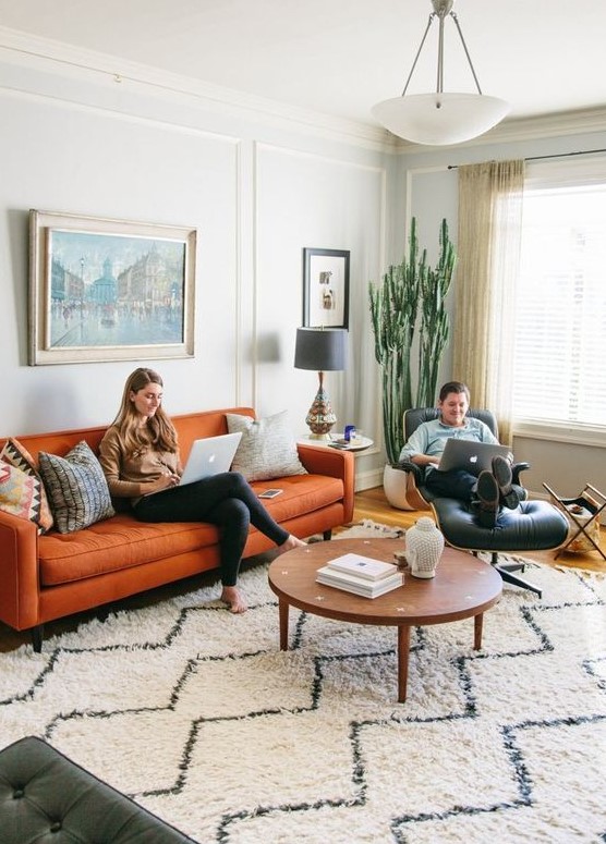 a mid-century boho living room done in neutrals, with a modern orange sofa and a black leather chair plus a statement cactus and artworks