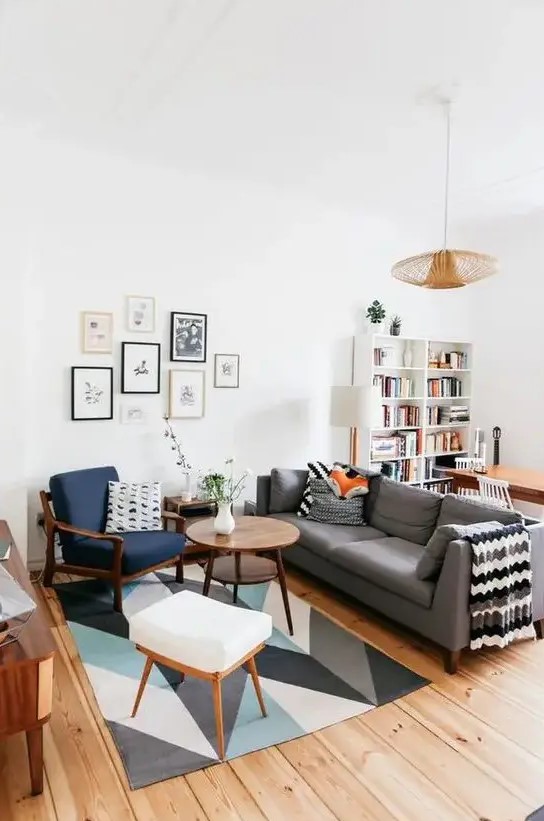 a mid century modern living room with a bold printed rug, a grey sofa, a navy chair and a white stool, a cool gallery wall