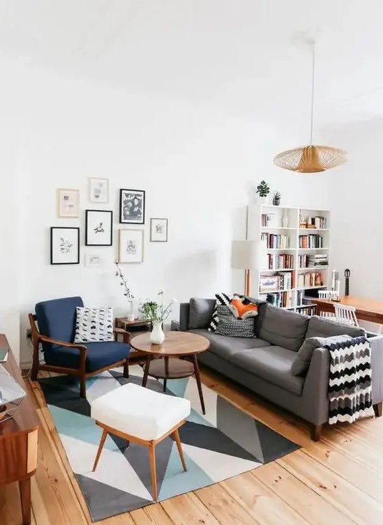 a mid-century modern living room with a bold printed rug, a grey sofa, a navy chair and a white stool, a cool gallery wall