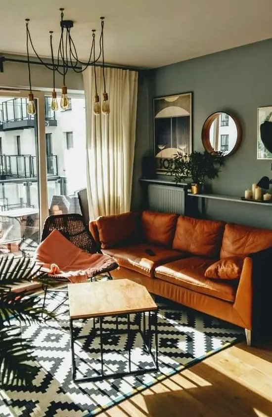 a mid-century modern living room with grey walls, an amber leather sofa, a black woven chair, an open shelf with decor and mirrors