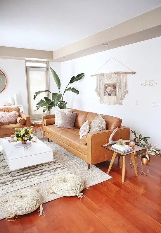 a mid-century modern to boho living room with tan leather furniture, a low white coffee table, woven poufs, a macrame hanging and potted plants