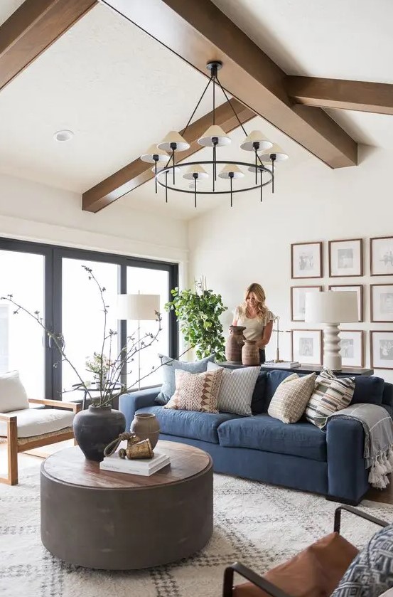 a modern farmhouse neutral living room with a modern blue sofa, a gallery wall, a round coffee table and mismatching chairs, a stylish chandelier
