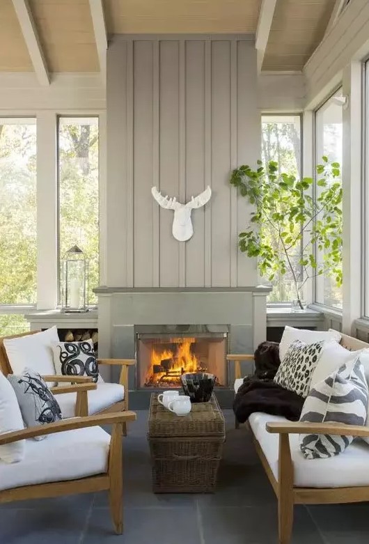 a modern farmhouse sunroom nook with a fireplace, wooden furniture with white upholstery, greenery and a skull