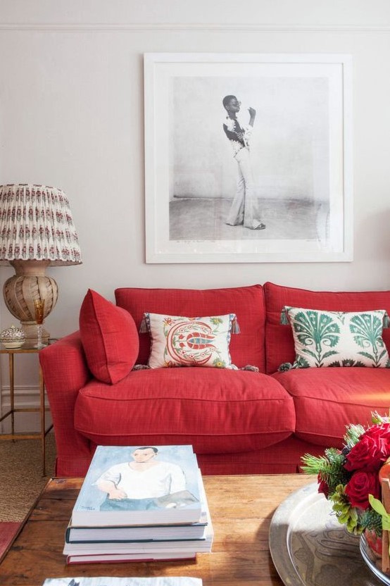 a modern living room with a bold red sofa, printed pillows, a statement artwork, a printed lamp and stacks of books
