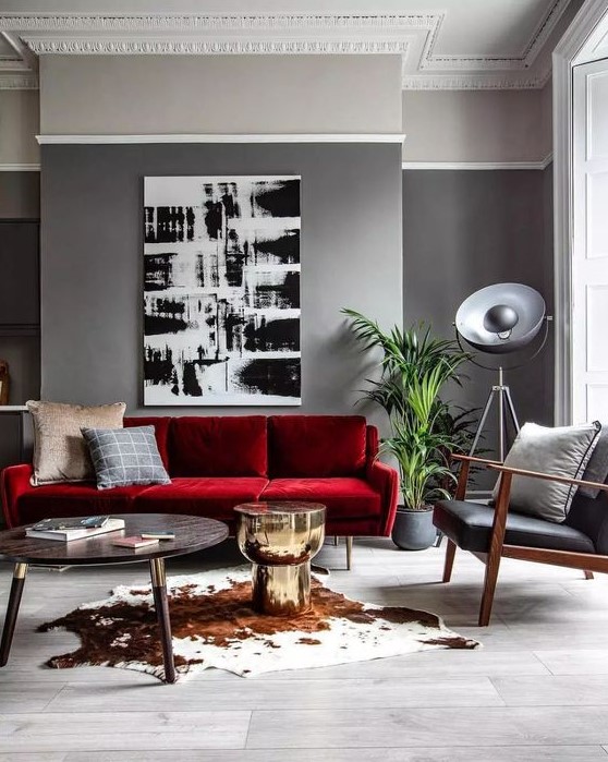 a modern living room with grey walls, a mid-century modern red sofa, a black leather chair, a monochromatic artwork and a round table