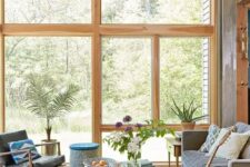 a modern sunroom with a grey sofa, black leather chairs, a low coffee table, potted plants and colorful pillows and blankets