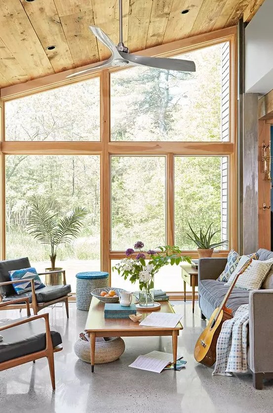 a modern sunroom with a grey sofa, black leather chairs, a low coffee table, potted plants and colorful pillows and blankets